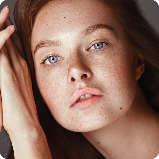 Close-up portrait of a young woman with freckled skin touching her hair