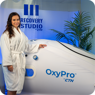 Woman in a robe beside an OxyPro by CTN hyperbaric oxygen chamber
