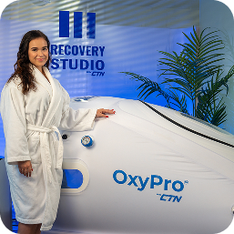 Person in a robe beside an OxyPro hyperbaric oxygen chamber